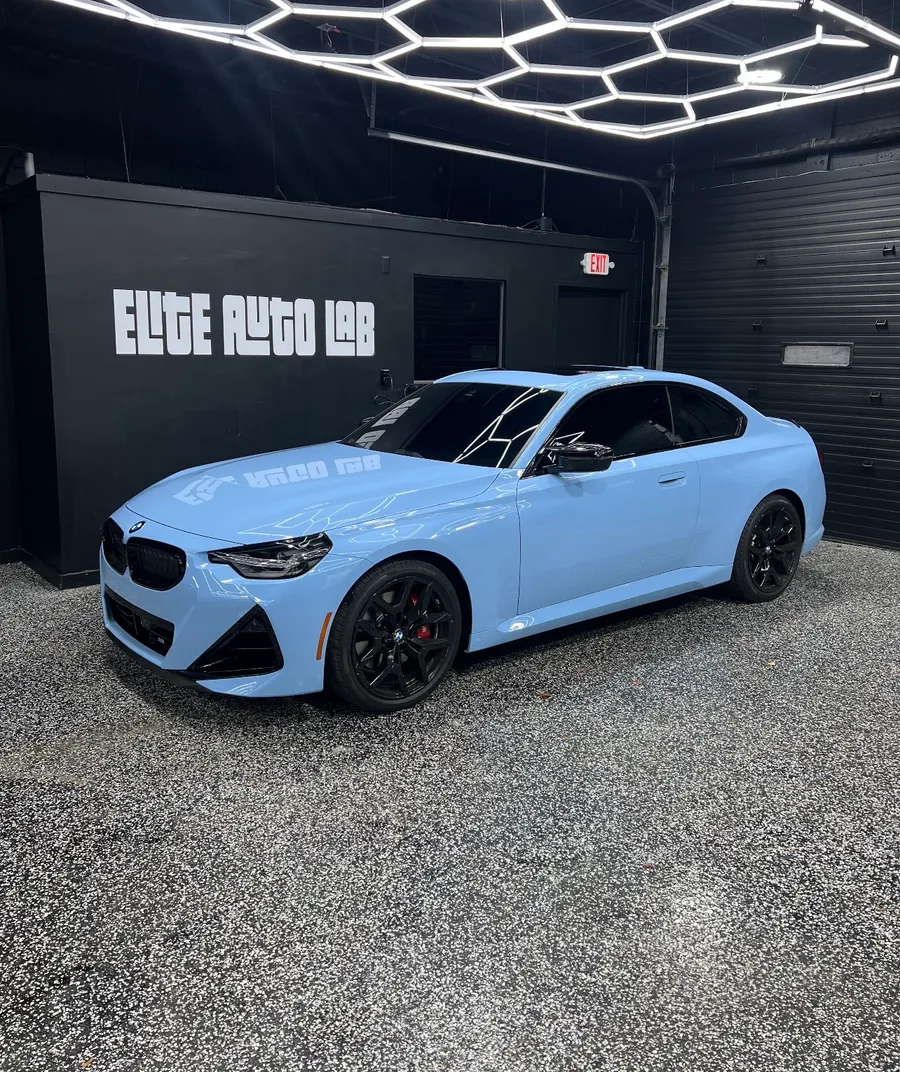Light blue BMW 2 Series coupe in front of the Elite Auto Lab sign in the shop in Madison Heights, a paint protection film job